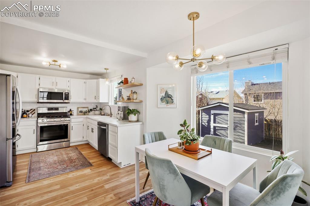 Image 10 of 27: Kitchen with hanging light fixtures, stainless steel appliances, white cabi