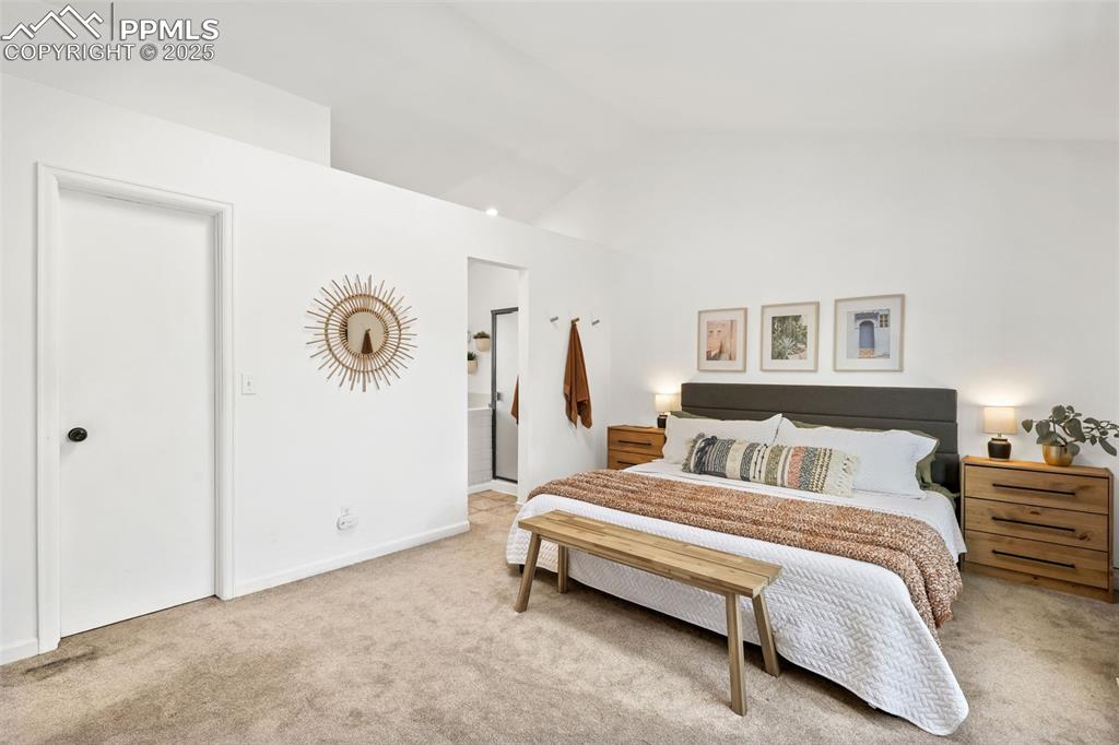 Image 14 of 27: Bedroom with vaulted ceiling, carpet flooring, and ensuite bathroom