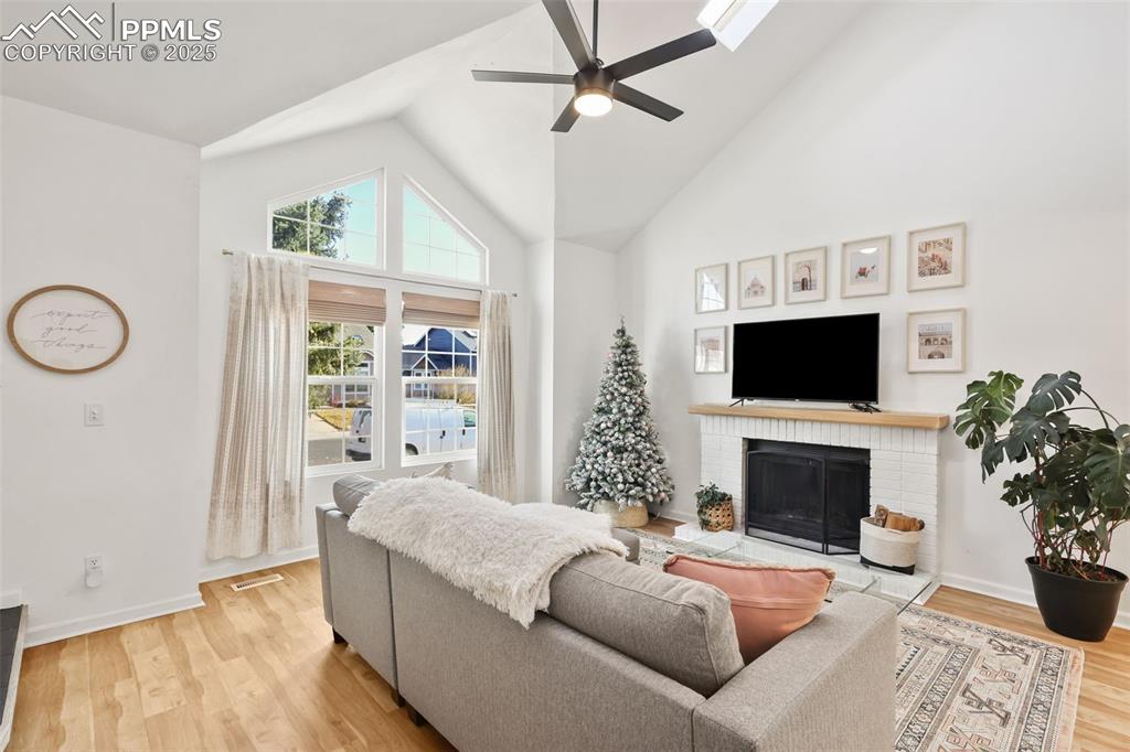 Image 4 of 27: Living area featuring high vaulted ceiling, light wood-style floors, a bric