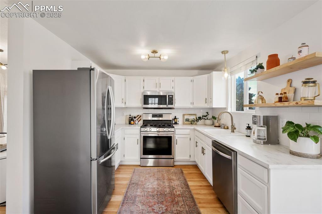 Image 9 of 27: Kitchen with stainless steel appliances, white cabinetry, open shelves, lig