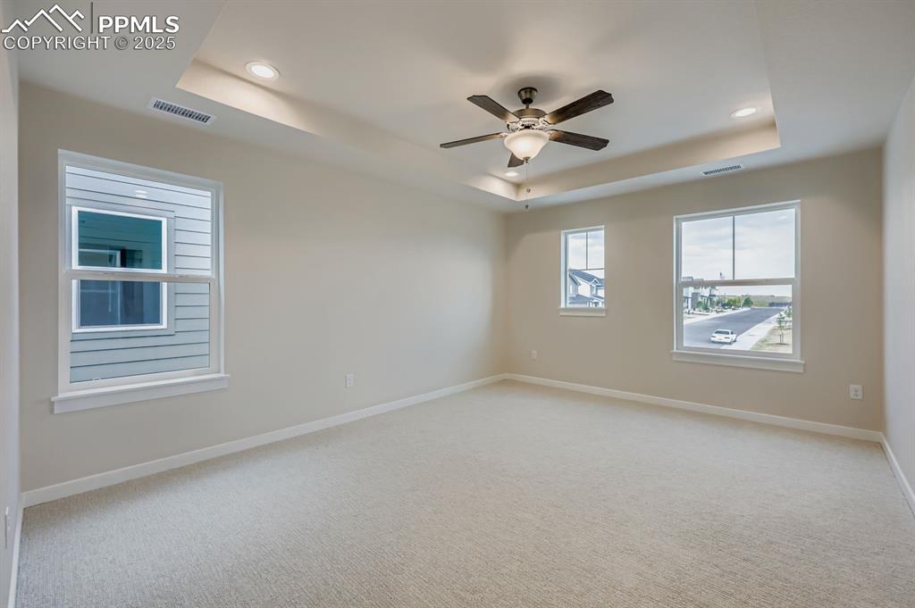 Image 12 of 28: Unfurnished room with a raised ceiling, light carpet, ceiling fan, and rece