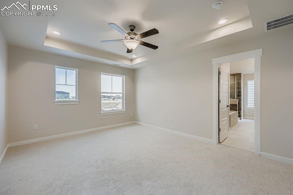 Image 14 of 28: Unfurnished bedroom with a raised ceiling, light carpet, a ceiling fan, ens
