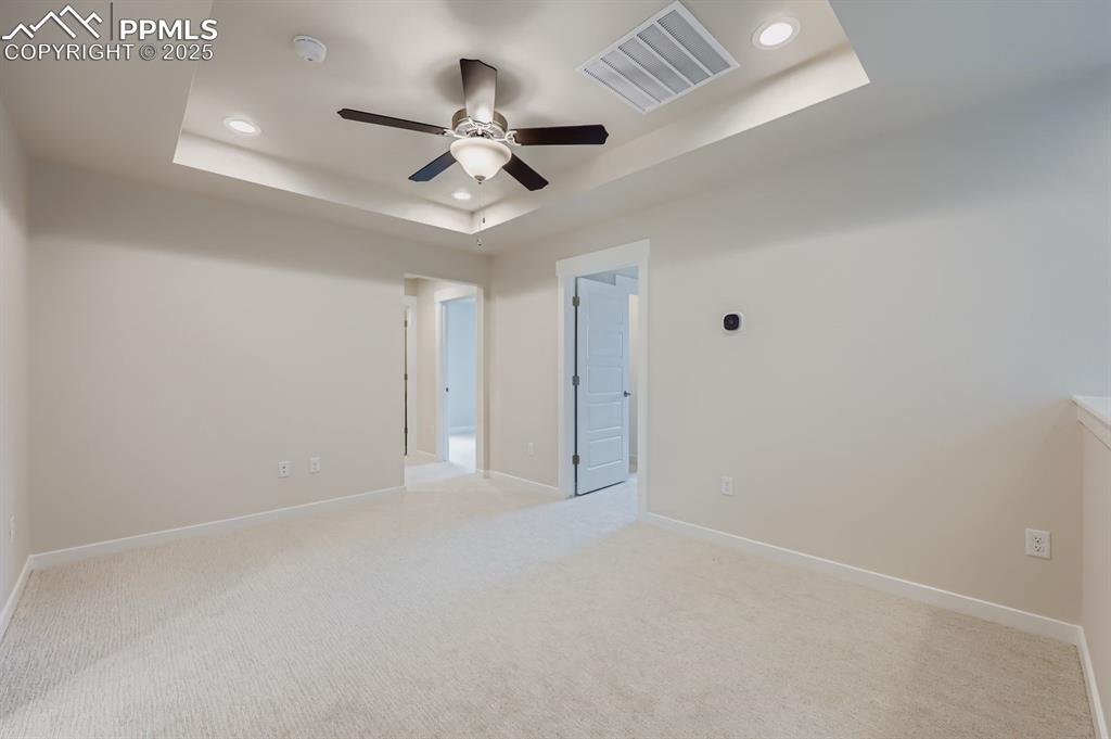 Image 23 of 28: Unfurnished bedroom with a raised ceiling, light carpet, a ceiling fan, and