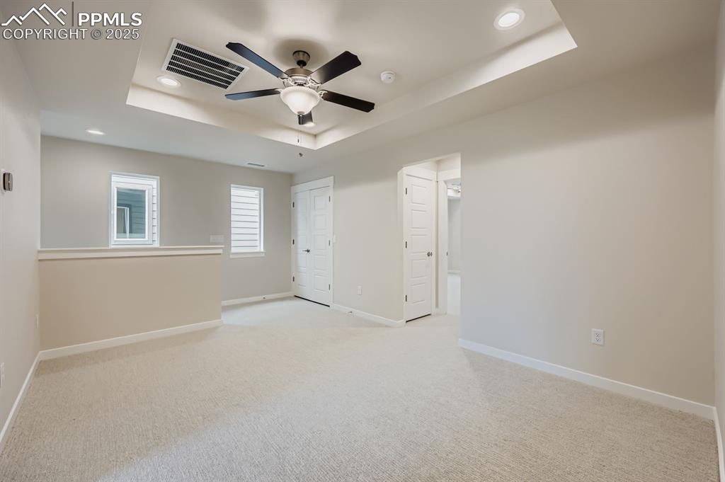Image 24 of 28: Empty room with a raised ceiling, light carpet, ceiling fan, and recessed l