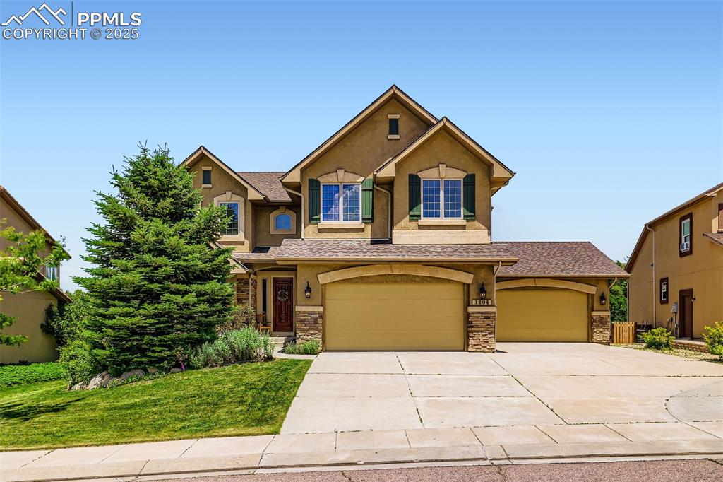 Caption: View of front of home with stucco siding, driveway, an attached 4-car garage, and stone siding