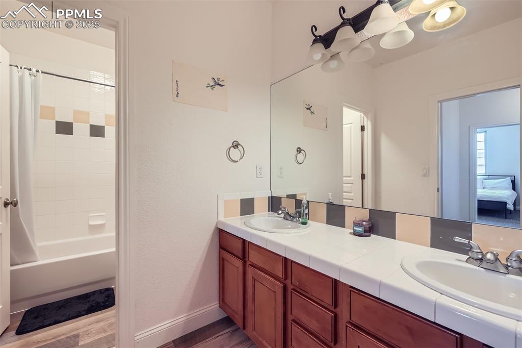 Image 17 of 28: Bathroom with double vanity, shower / tub combo with curtain, and faux wood