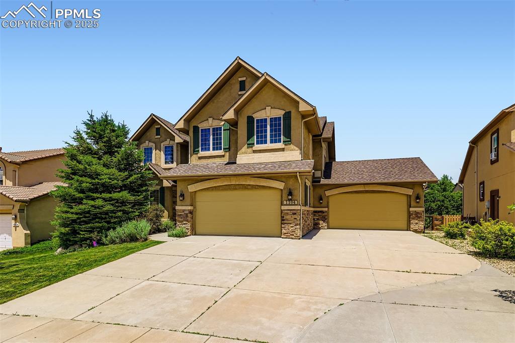 Image 3 of 28: View of front of house with stucco siding, stone siding, driveway, and an a