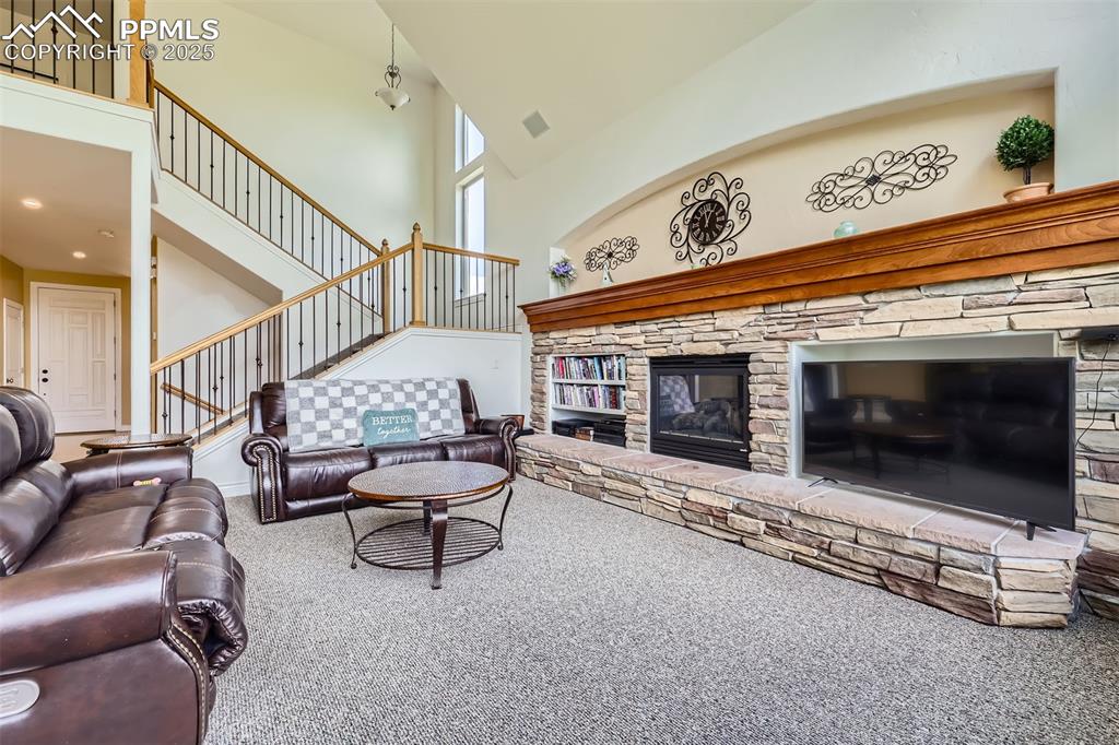 Image 5 of 28: Carpeted living area with a high ceiling, a fireplace, and stairway