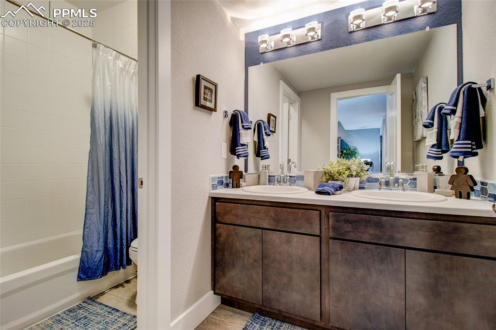 Image 28 of 30: Full bathroom featuring double vanity, a textured wall, shower / bath combo