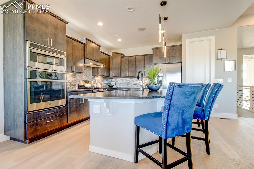 Image 7 of 30: Kitchen with tasteful backsplash, a kitchen bar, stainless steel appliances