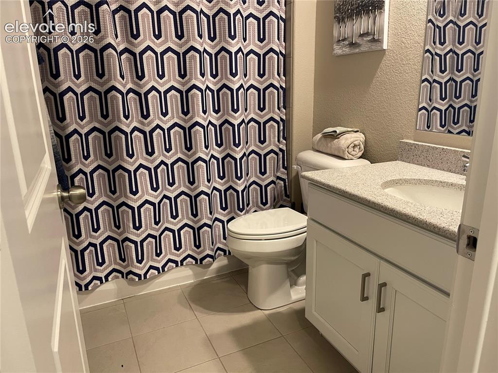 Image 17 of 25: Full bath with a textured wall, vanity, and light tile patterned flooring