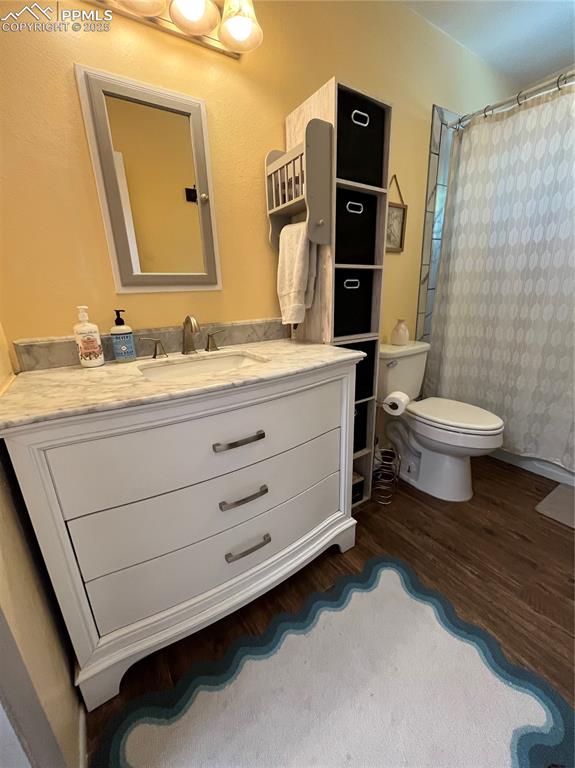 Image 16 of 29: Full bathroom with wood finished floors, toilet, vanity, and curtained show