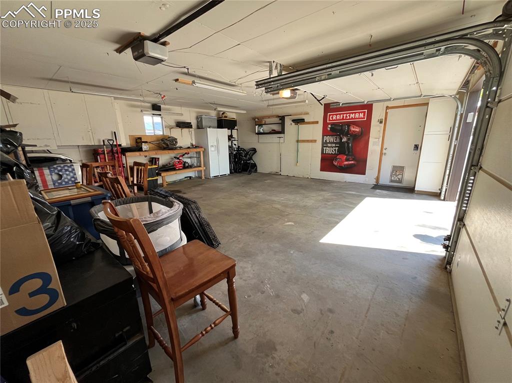 Image 27 of 29: Garage featuring a garage door opener and white refrigerator with ice dispe