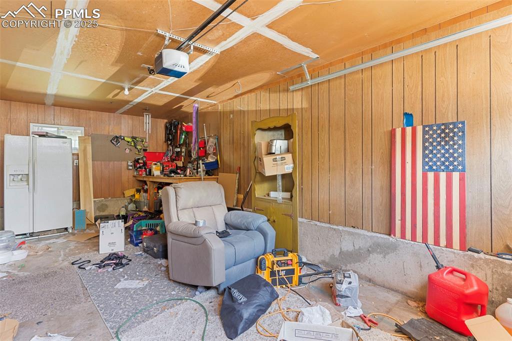 Image 21 of 25: Garage with white fridge with ice dispenser, wooden walls, a garage door op