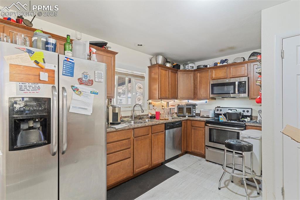 Image 8 of 25: Kitchen featuring stainless steel appliances, brown cabinetry, and light fl