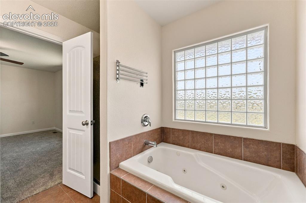 Image 16 of 50: Jetted soaking tub with tile surround, glass block privacy window, chrome p
