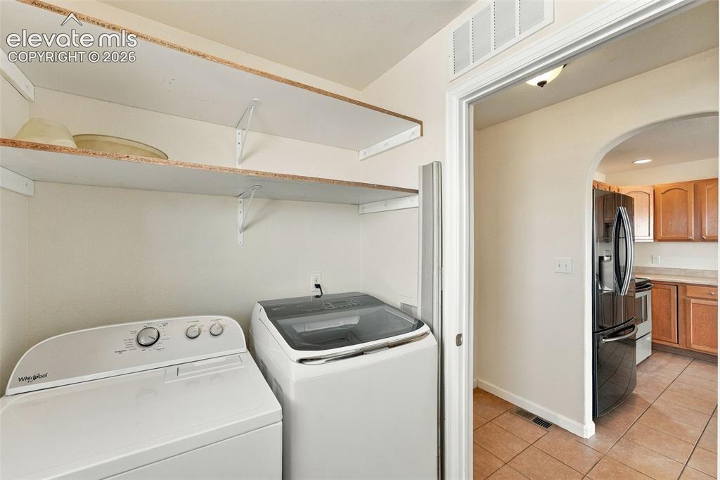 Image 21 of 50: Laundry area featuring open wall-mounted shelving, neutral walls, and tile 