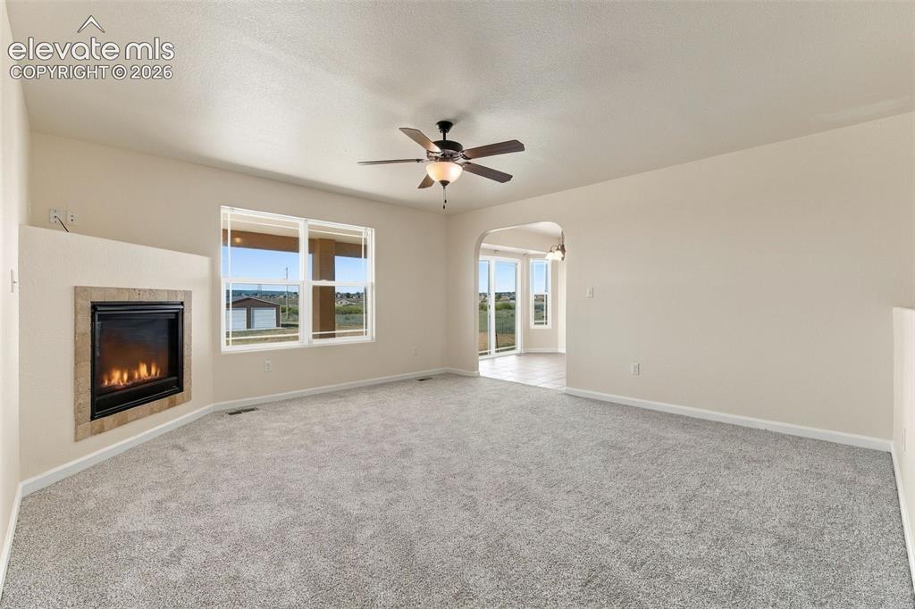 Image 3 of 50: Fireplace with a stone surround, neutral wall-to-wall carpeting, ceiling fa