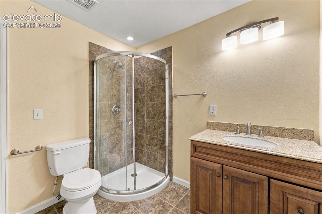 Image 33 of 50: Corner shower with glass enclosure and tiled surround, wood-finish vanity w