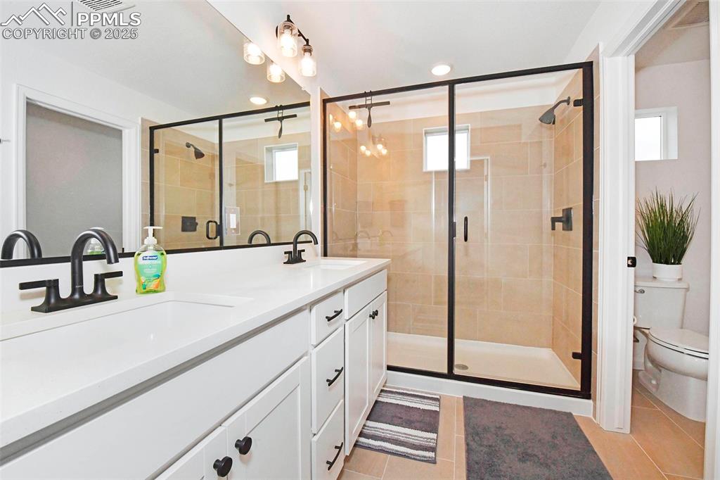 Image 19 of 26: Bathroom with double vanity, light tile patterned floors, a stall shower, a