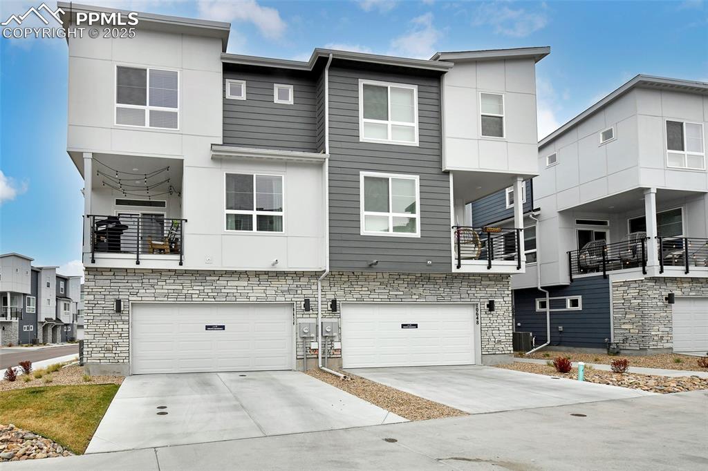 Image 2 of 26: Rear view of property with a balcony, concrete driveway, an attached garage