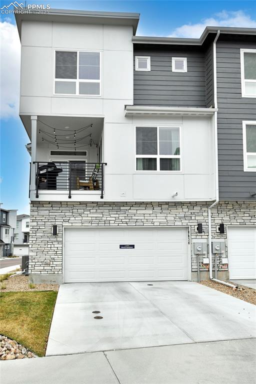 Image 4 of 26: View of front of property with a balcony, a garage, driveway, stone siding,