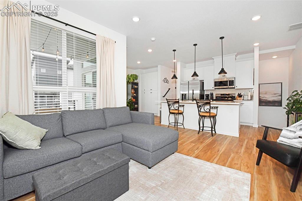 Image 6 of 26: Living area with light wood finished floors and recessed lighting