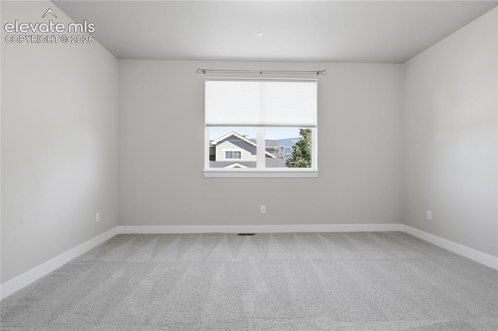 Image 25 of 28: Window with roller shade, gray carpet flooring, and neutral wall paint