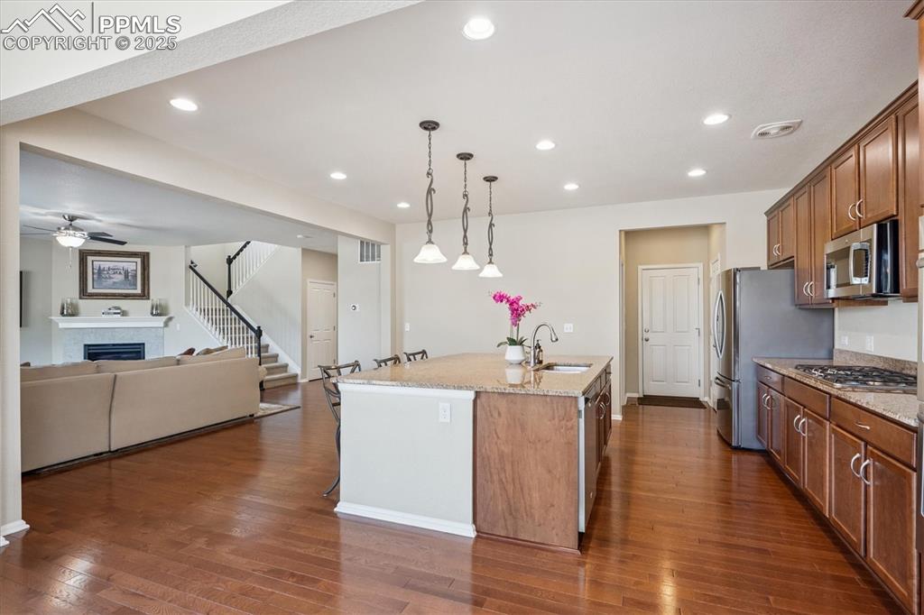 Image 13 of 36: Kitchen with an island with sink, brown cabinetry, dark wood finished floor