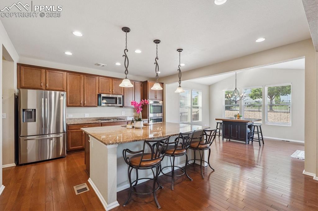 Image 9 of 36: Kitchen featuring stainless steel appliances, brown cabinets, dark wood-sty