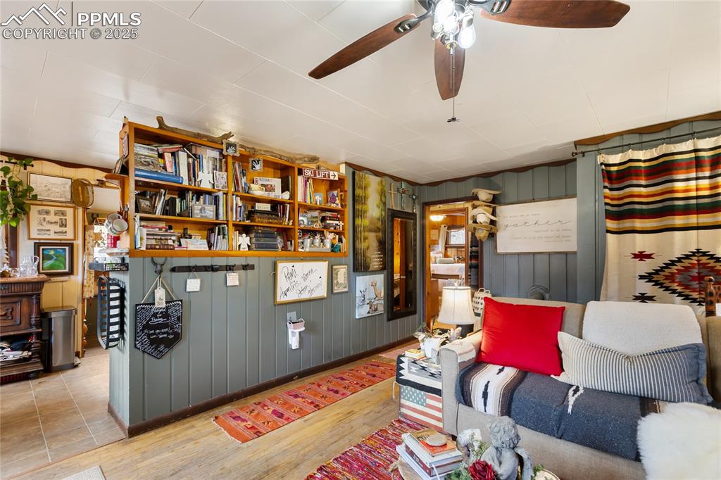 Image 16 of 47: Living room with wood finished floors, wooden walls, and a ceiling fan