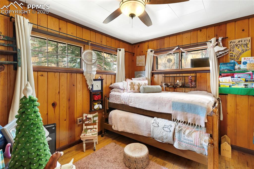 Image 29 of 47: Bedroom with wood walls, wood finished floors, and ceiling fan