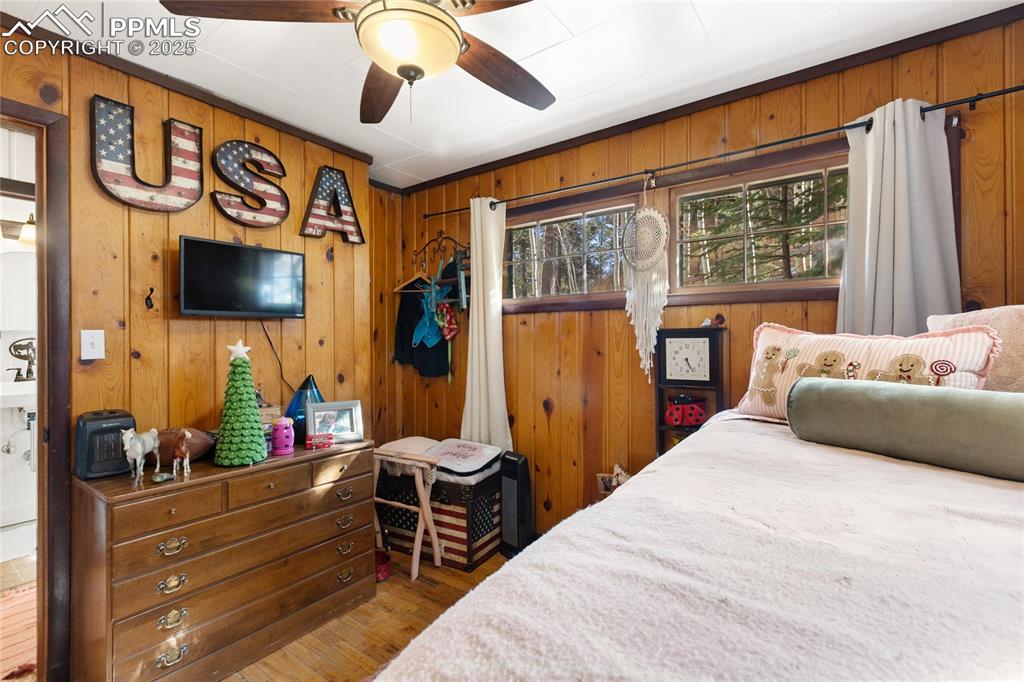 Image 30 of 47: Bedroom featuring wooden walls, wood finished floors, and ceiling fan