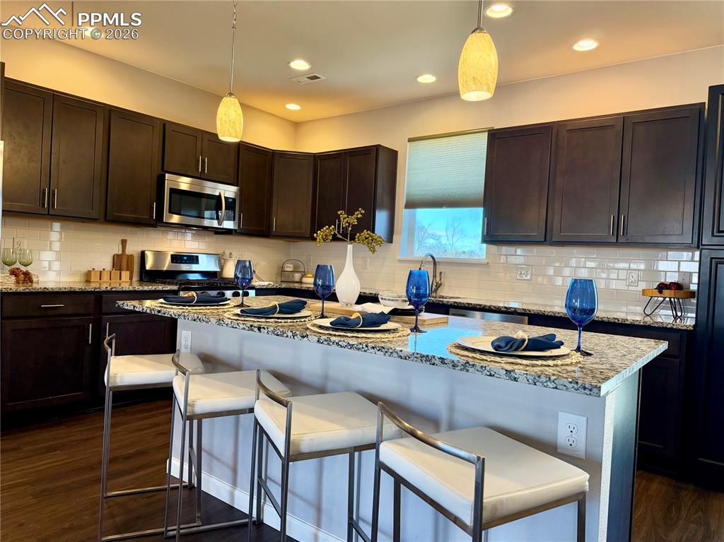 Image 10 of 41: Kitchen featuring dark brown cabinets, light stone counters, a kitchen brea