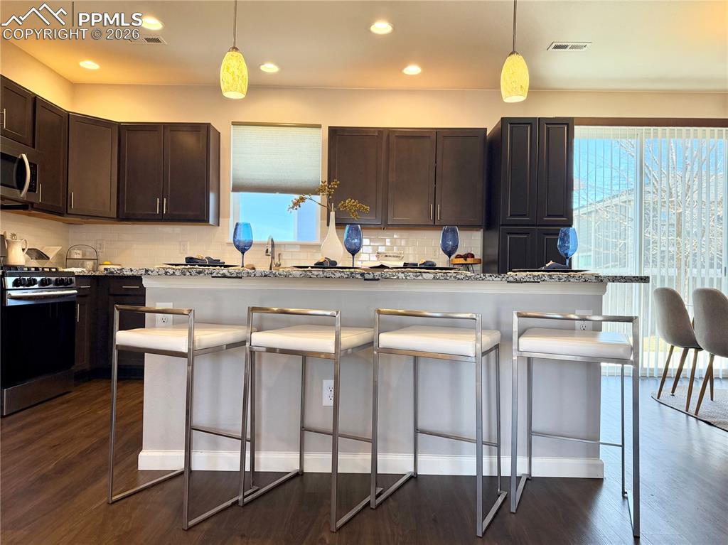 Image 8 of 41: Kitchen with dark brown cabinetry, a breakfast bar area, appliances with st