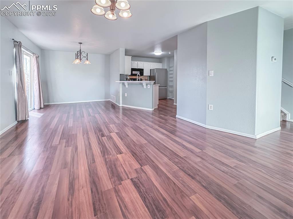 Image 6 of 27: Unfurnished living room with hanging lights and dark wood-type flooring