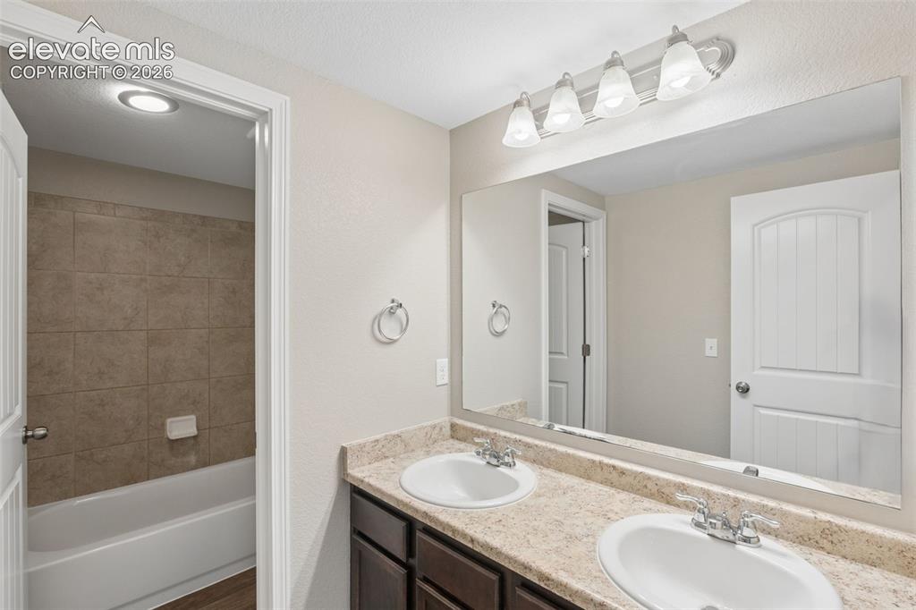Image 34 of 46: Bathroom in basement featuring a dual sink vanity with a speckled counterto