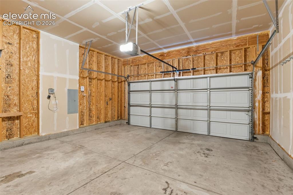 Image 42 of 46: Concrete floor garage with a sectional overhead door and an automatic opene