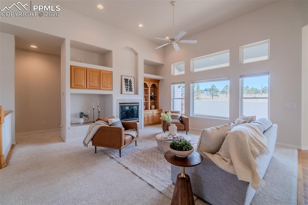 Image 16 of 50: Living room with a high ceiling, built in features, a ceiling fan, a glass 
