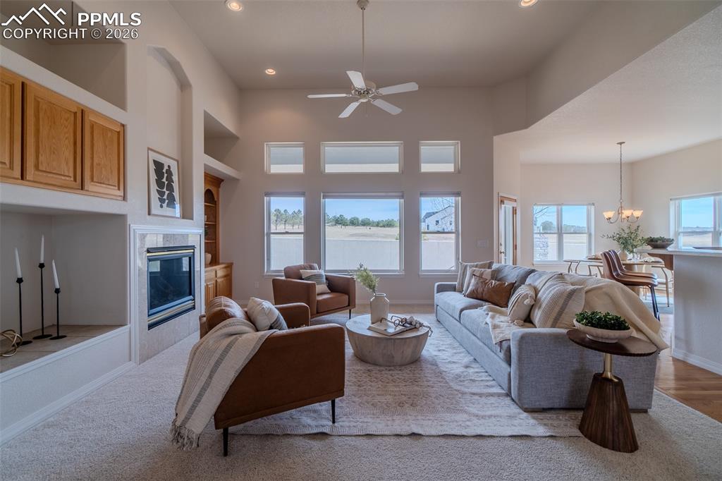 Image 17 of 50: Living room with a ceiling fan, built in features, a high ceiling, a chande