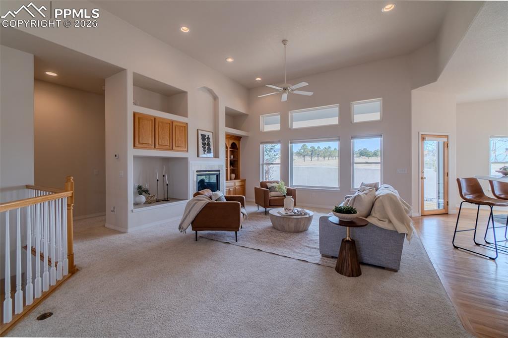 Image 19 of 50: Living room with a high ceiling, built in features, a ceiling fan, a glass 