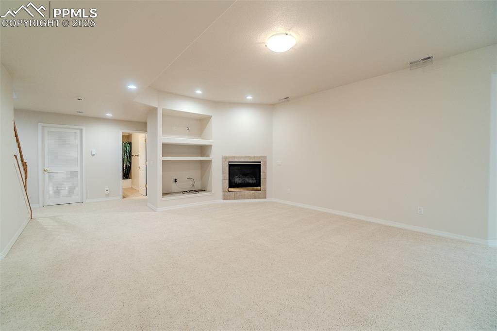 Image 31 of 50: 2nd living room with built in features, light carpet, a tiled fireplace, an