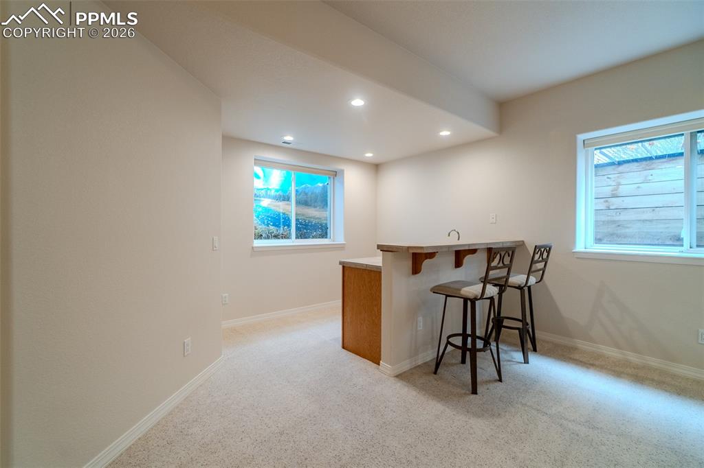 Image 33 of 50: Indoor wet bar with light colored carpet, recessed lighting, and light coun