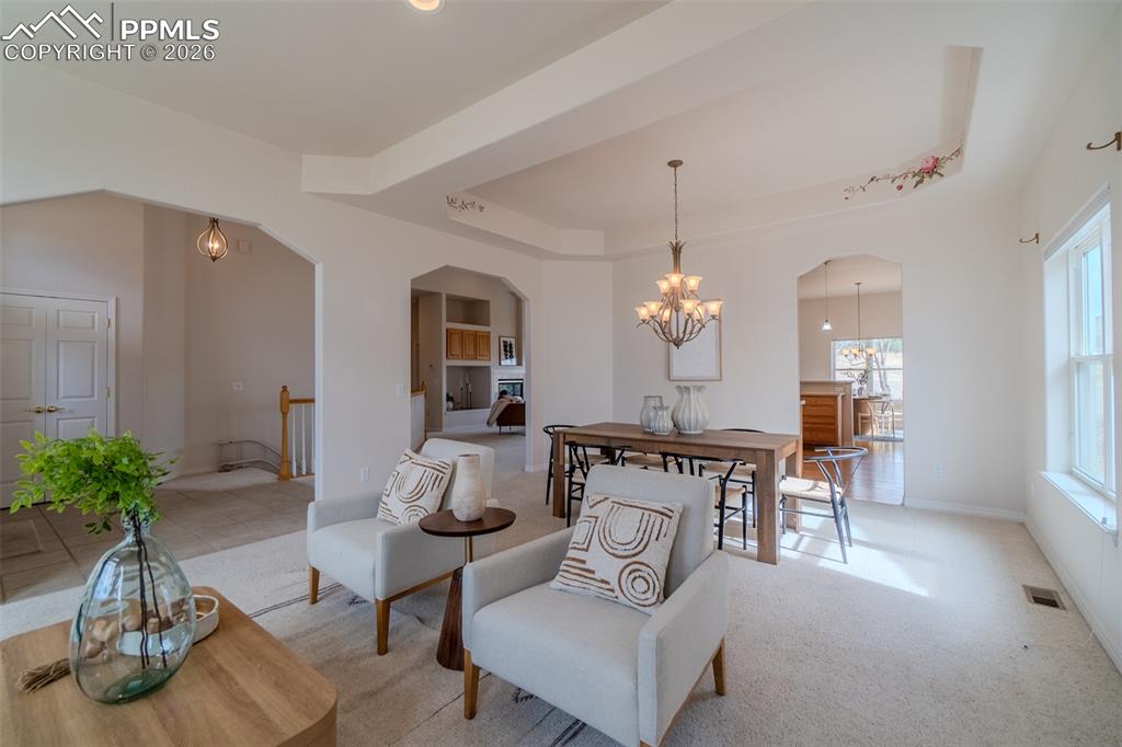 Image 4 of 50: Living area with a raised ceiling, arched walkways, carpet floors, and a ch