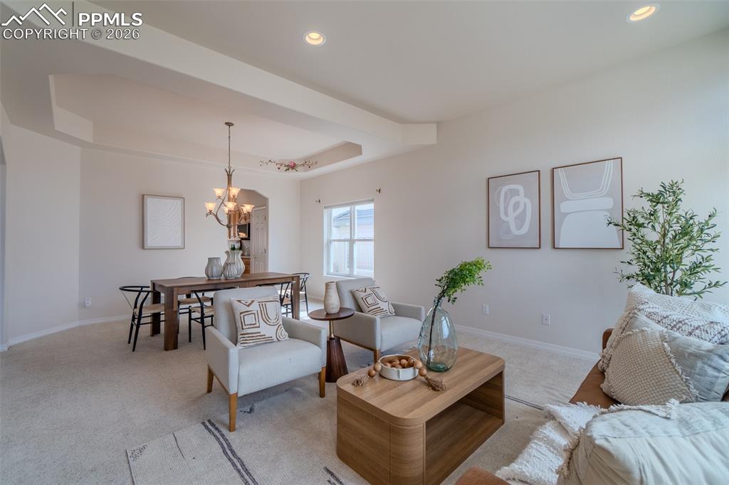 Image 6 of 50: Carpeted living room with a raised ceiling and a chandelier