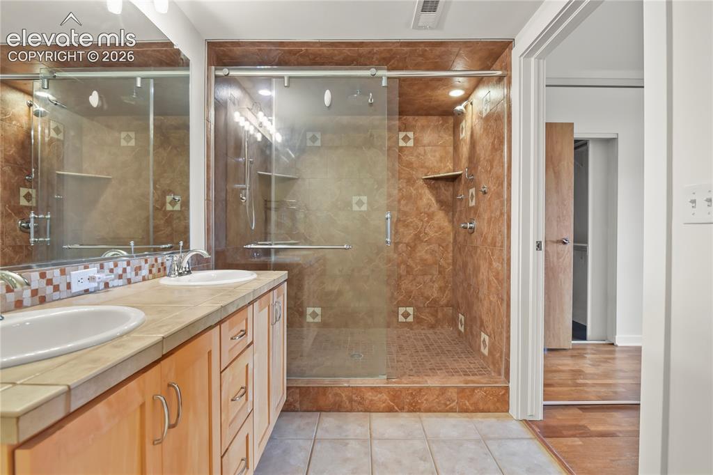 Image 14 of 50: En-suite bath showcasing dual sinks, tile flooring, and oversized shower