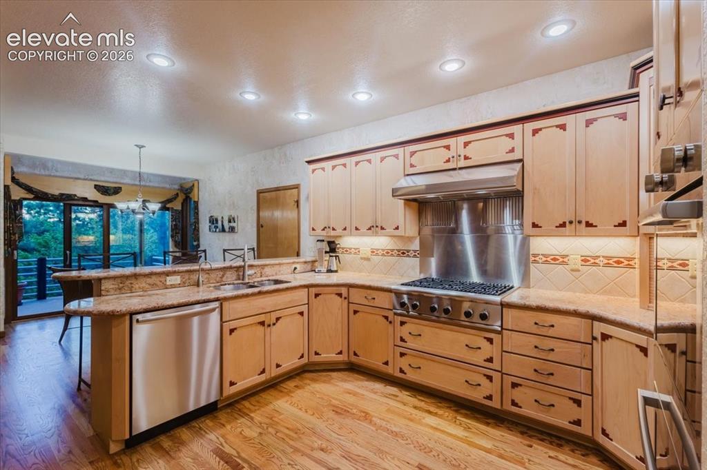 Image 11 of 50: U-shaped kitchen featuring light wood cabinetry with decorative inlays, gra