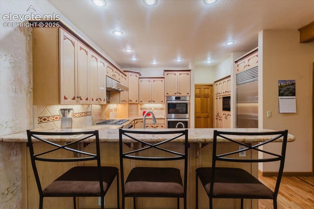 Image 13 of 50: Kitchen featuring an expansive breakfast bar with stone-finish countertop,