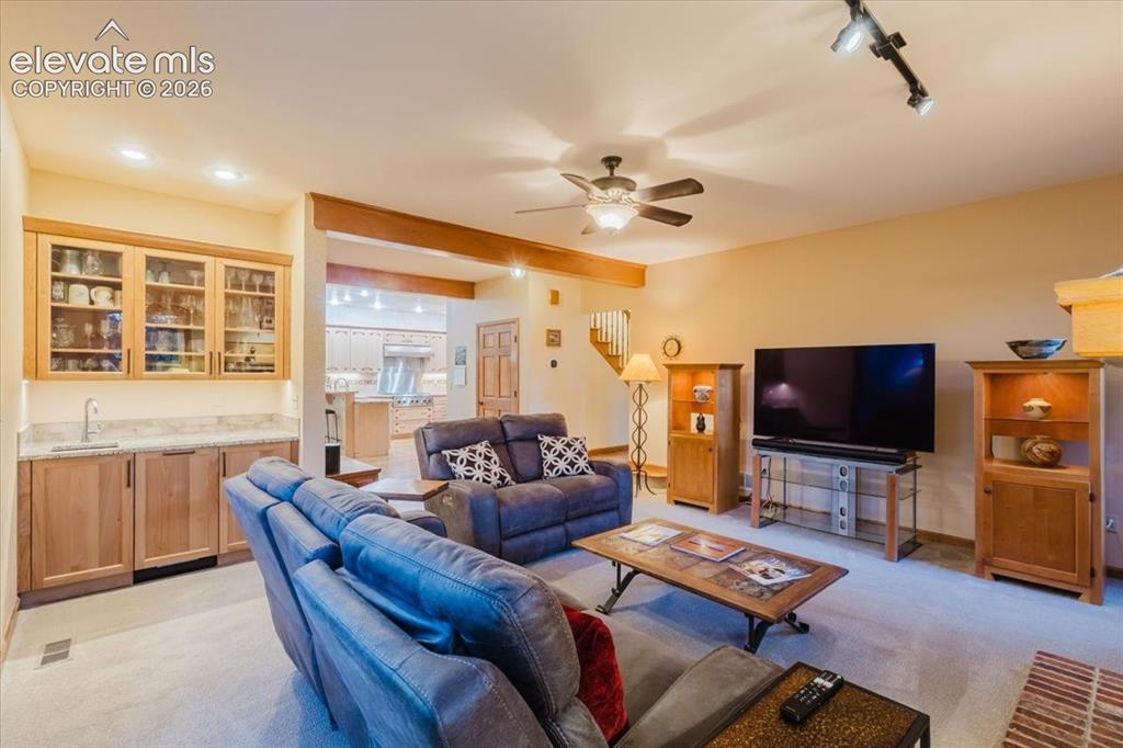 Image 19 of 50: Open-concept living area featuring a wet bar with glass-front cabinetry and