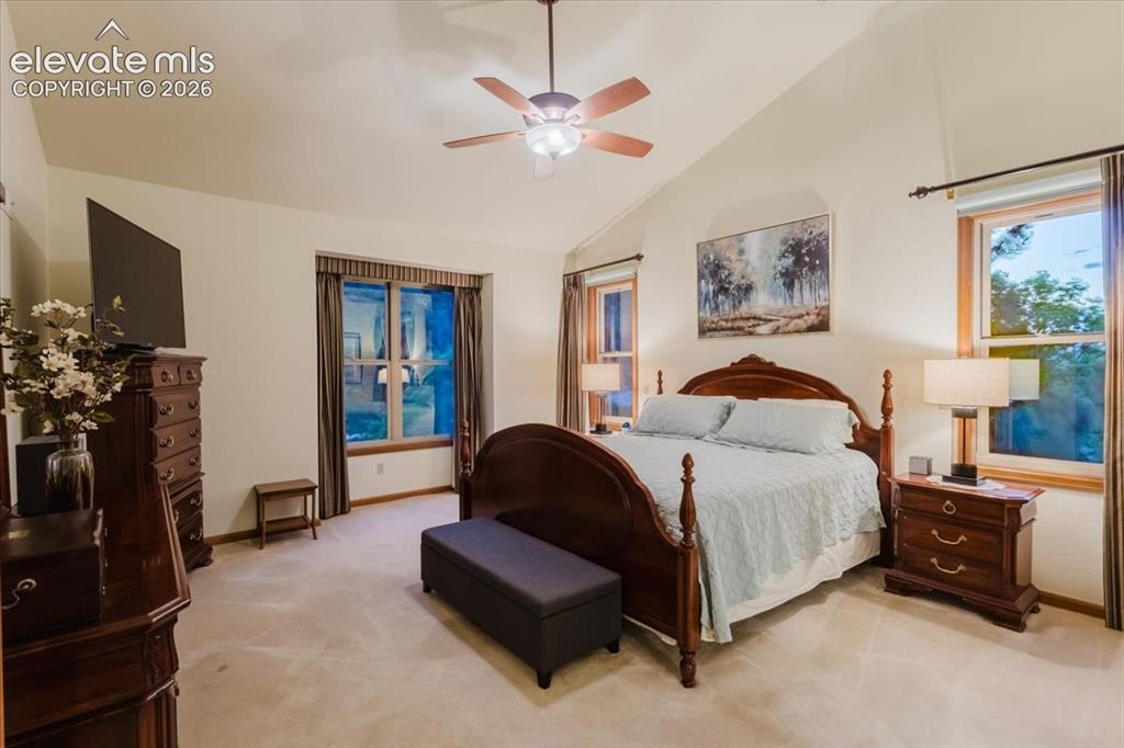 Image 23 of 50: Vaulted ceiling with a ceiling fan, two large windows with wood trim, wall-